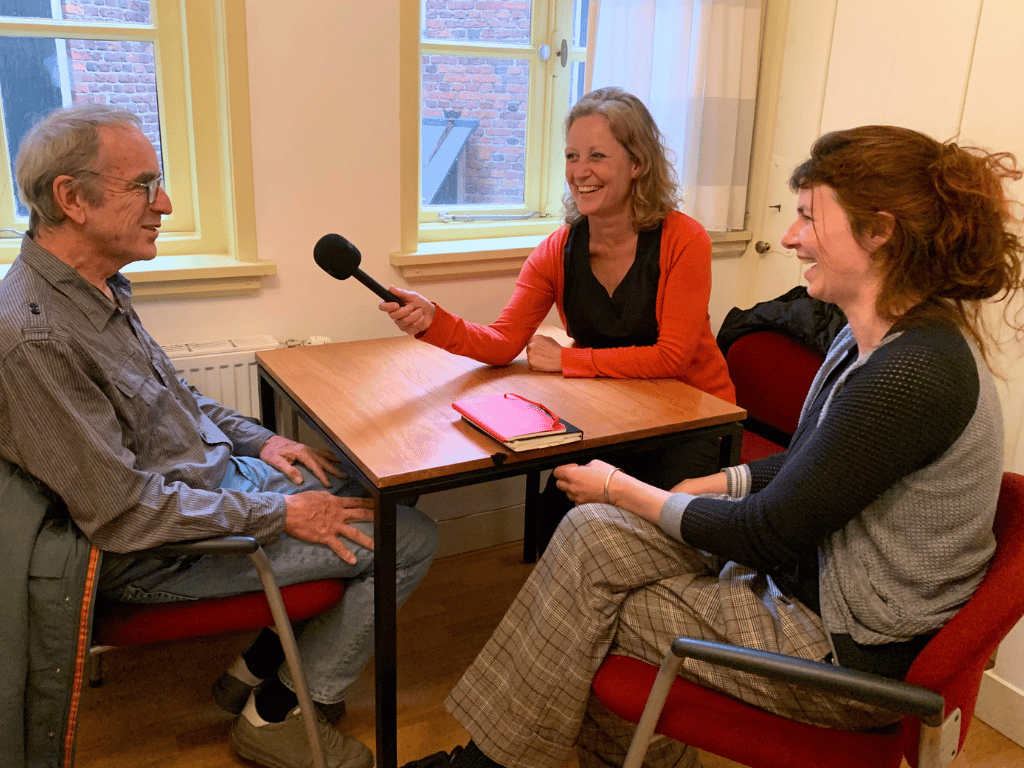 Twee personen waaronder Ieke Benschop die iemand interviewen voor een podcast.