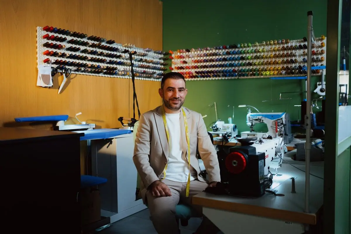 Een reparateur die in een naaiatelier zit en de camera inkijkt.