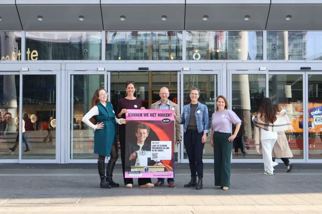 Betrokkenen van het project Heel Nederland Repareert die met een campagne poster poseren voor de ingang van het winkelcentrum Hoog Catharijne in Utrecht.