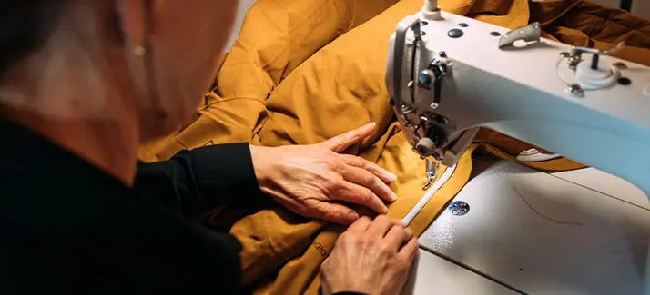 Een persoon die bezig is met het repareren van een jas met een naaimachine.