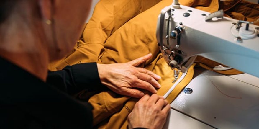 Een persoon die bezig is met het repareren van een jas met een naaimachine.