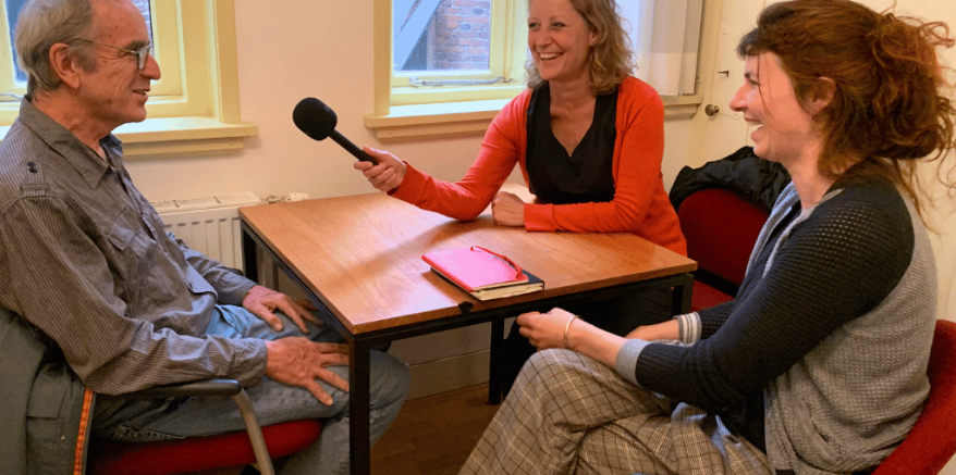 Twee personen waaronder Ieke Benschop die iemand interviewen voor een podcast.